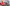 girl in pink hoodie wearing yellow snorkel and holding fishing net as sister dances with hula hoop and parents sit on sofa in surfing decorated caravan in Woolacombe