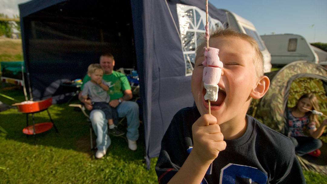 Boy eating toasted marshmallow by touring caravan with dad and brother in awning at Woolacombe holiday park