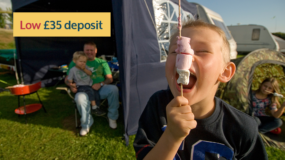 Boy eating toasted marshmallow by touring caravan with dad and brother in awning at Woolacombe holiday park
