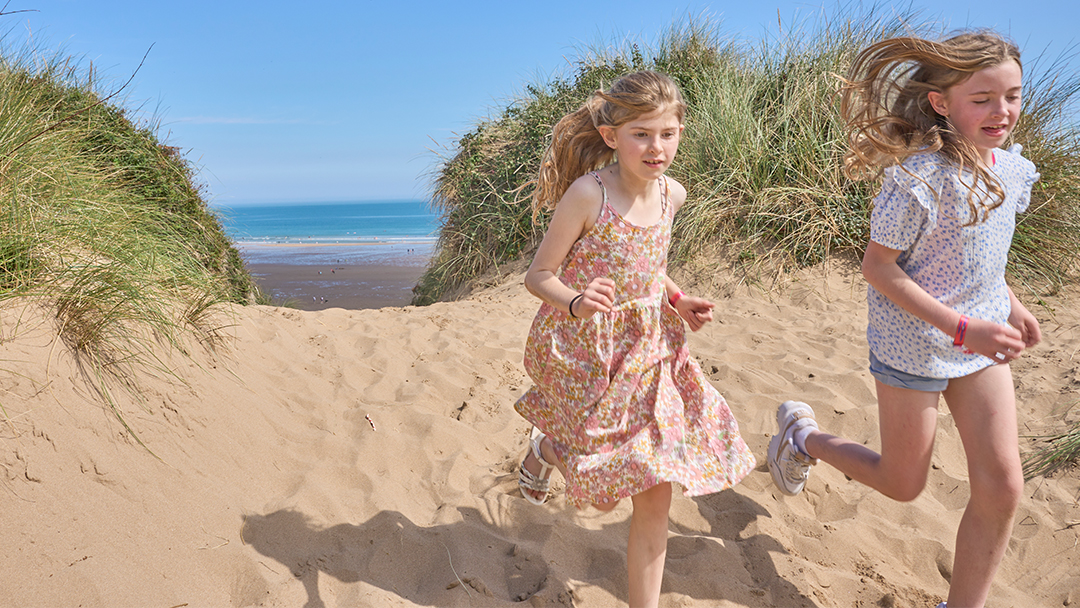 Two girls in summer beach wear running on the dunes at Woolacombe Sands